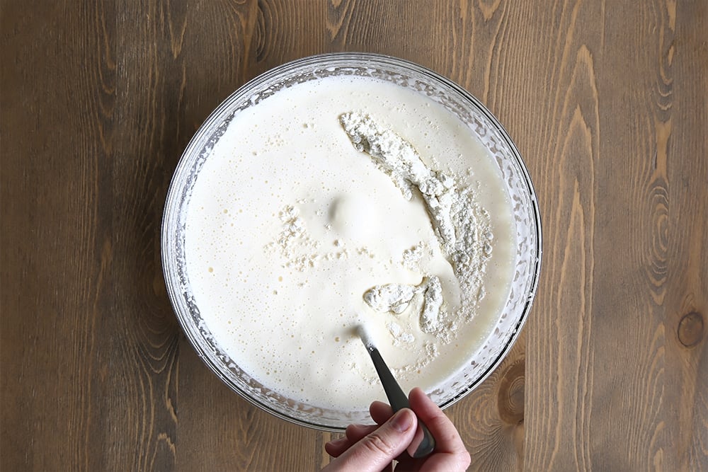 The whisked egg and sugar mix with added flour with a hand holding a spoon.