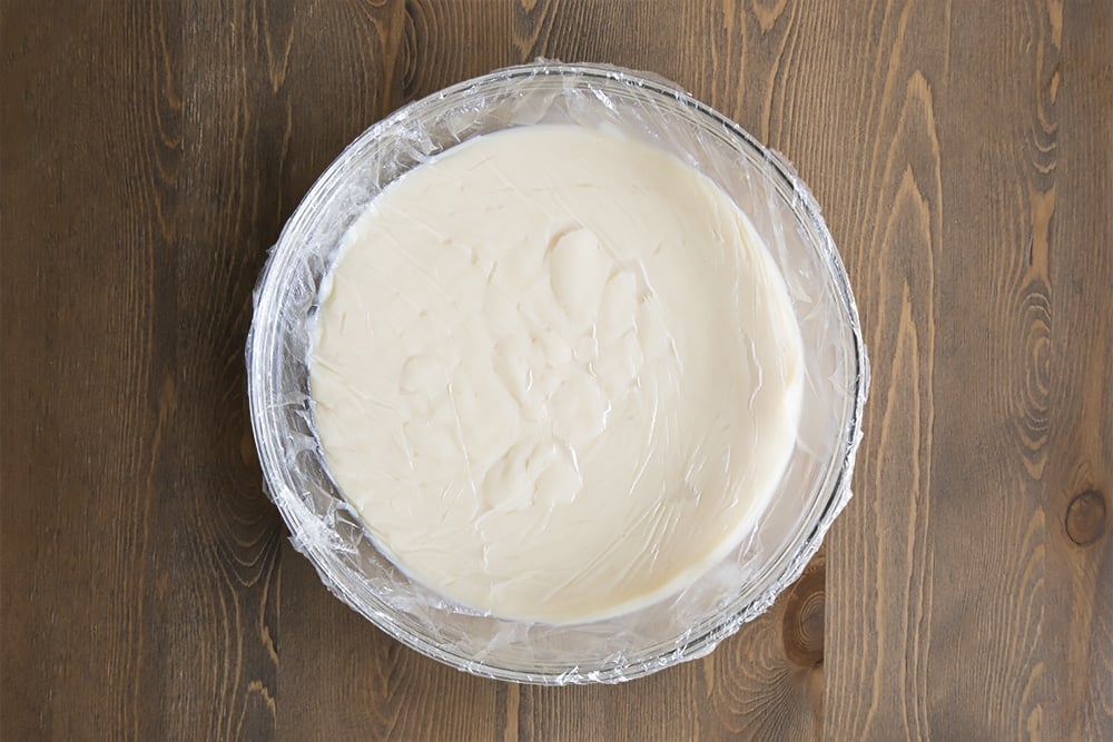 White egg mixture in a large clear bowl covered with plastic wrap.