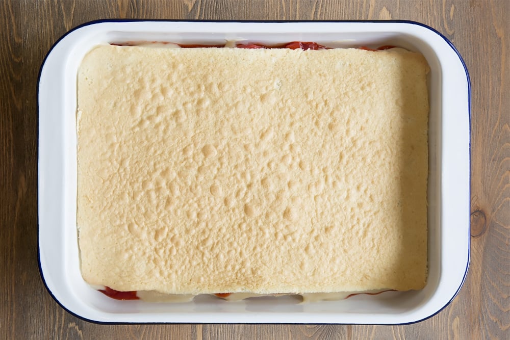 A white metal dish topped with a vanilla sponge layer.