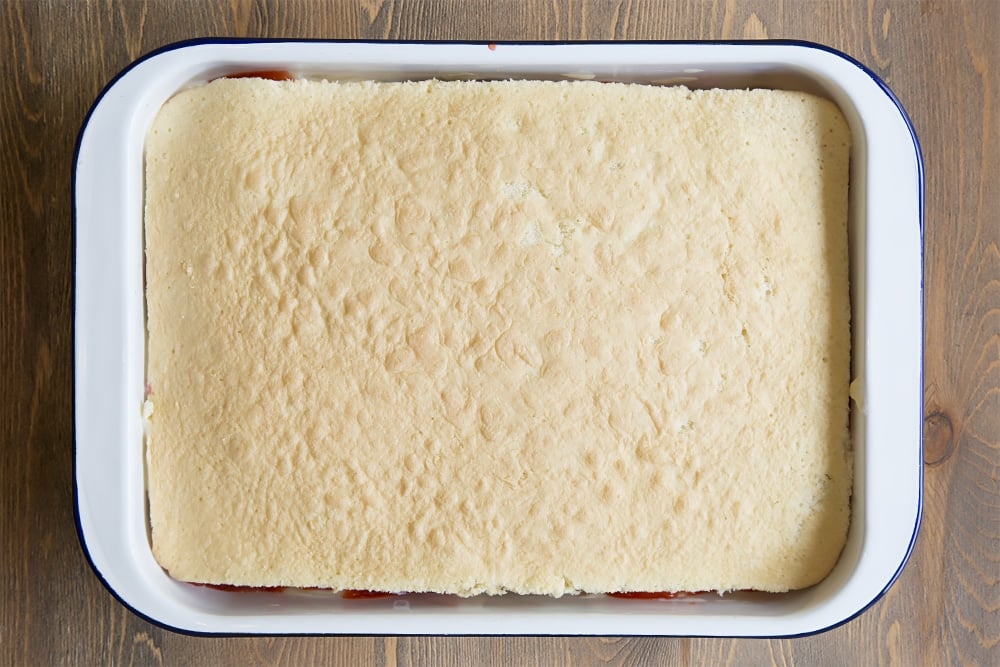 A white metal dish topped with a vanilla sponge layer.