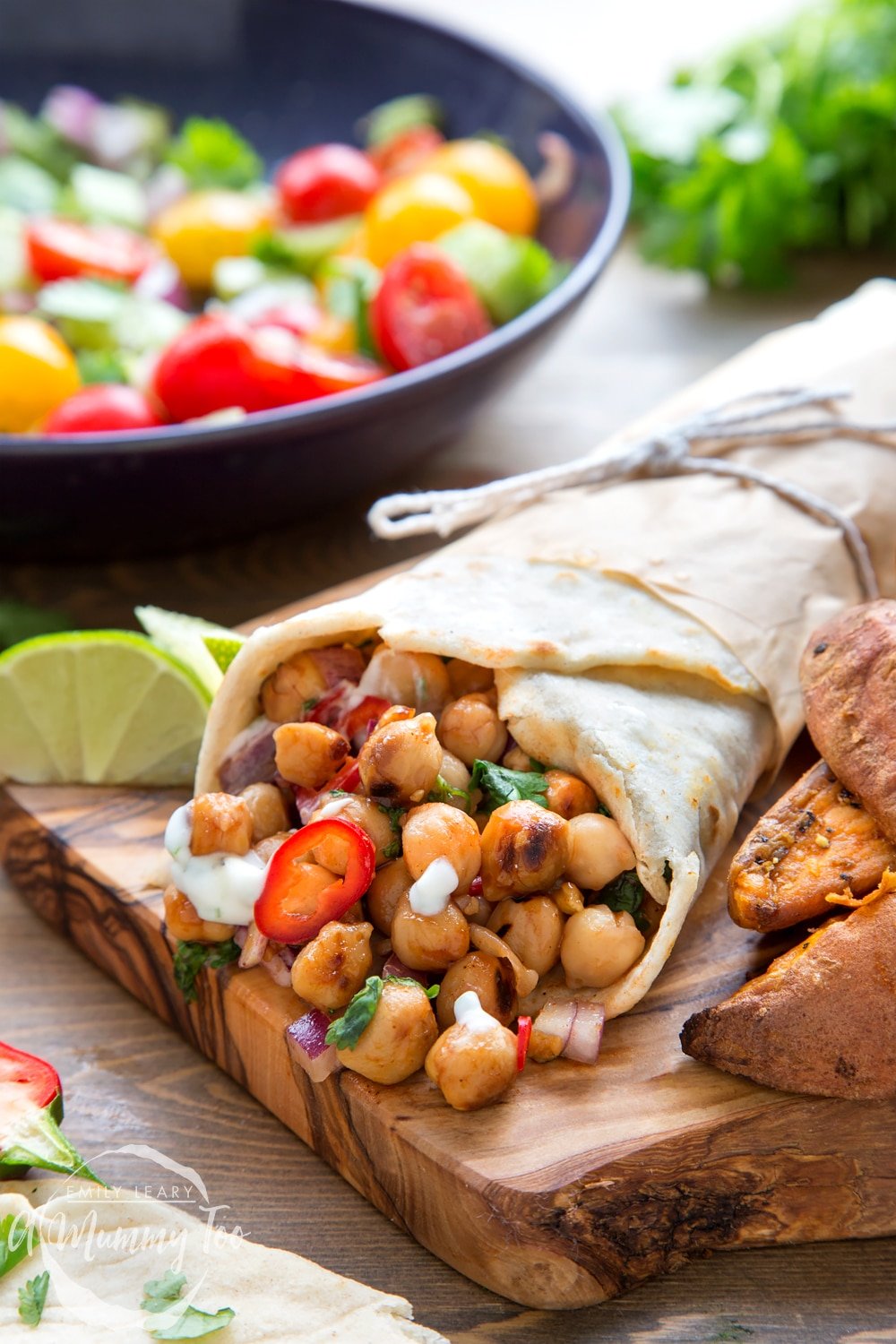 BBQ chickpea summer wraps, served on a chopping board alongside potato wedges and summery dressings. Discover how to create your own chickpea wraps in this recipe.