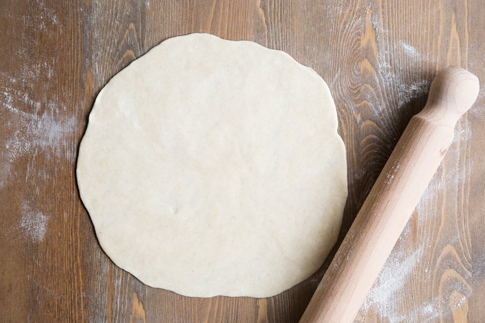 Tortilla dough rolled out flat into a circle, shown alongside a rolling pin