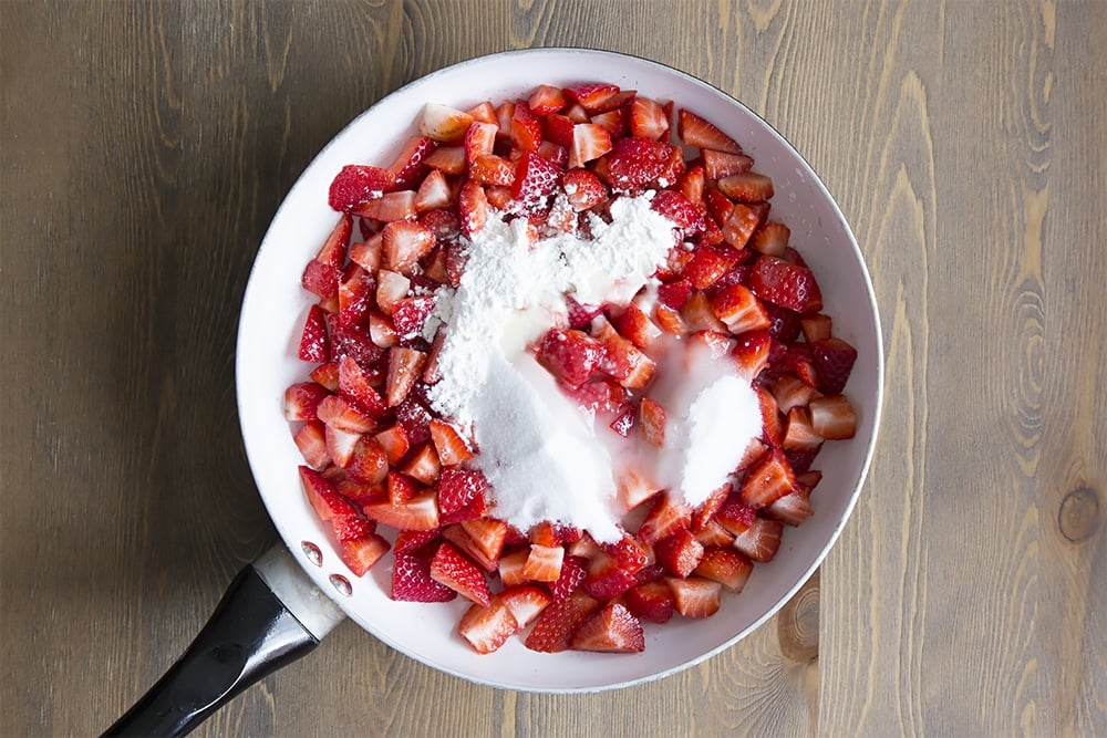 Strawberries, sugar, cornflour and lemon juice in a large saucepan on a wooden background.