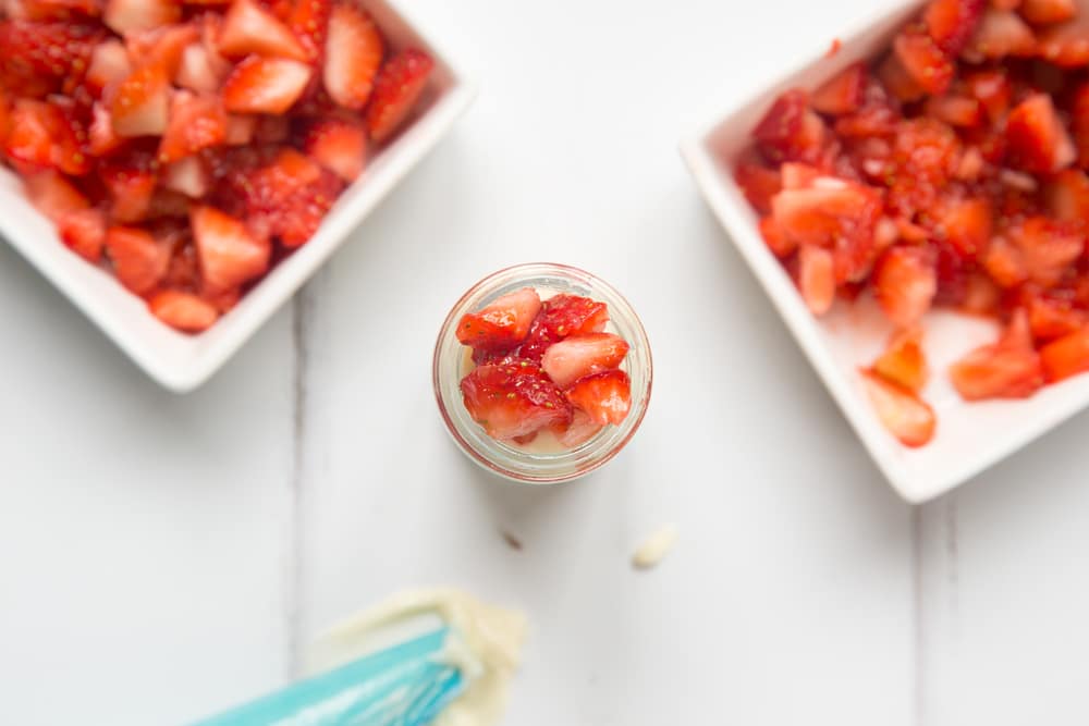 over head view of a small jar with chopped strawberries with two bowls of chopped strawberries at either side and a blue icing bag.