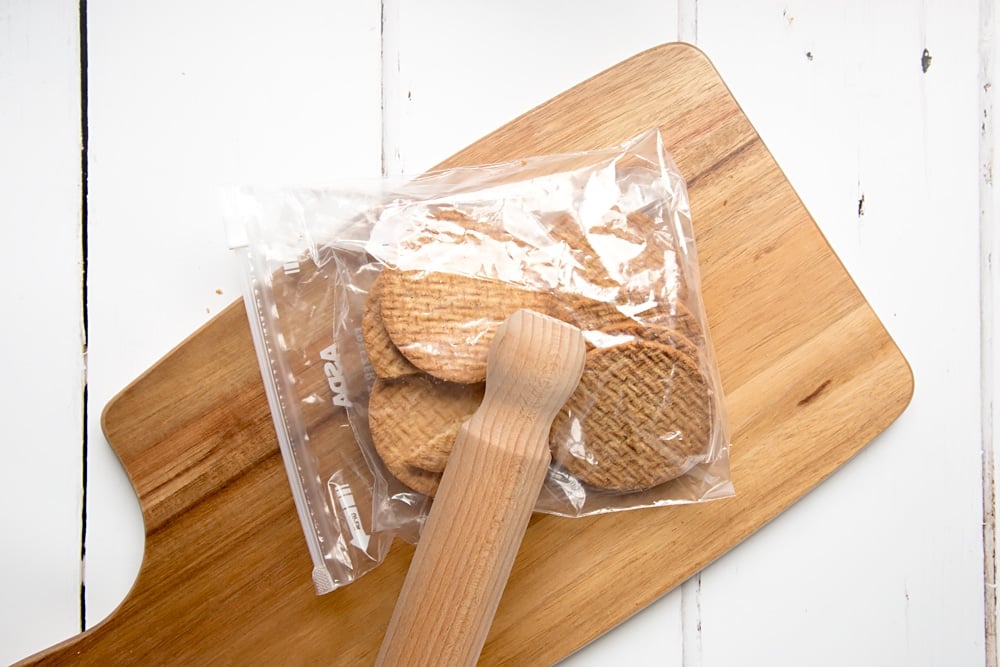 digestive biscuits in a food bag laid on a chopping board with a rolling pin on top.