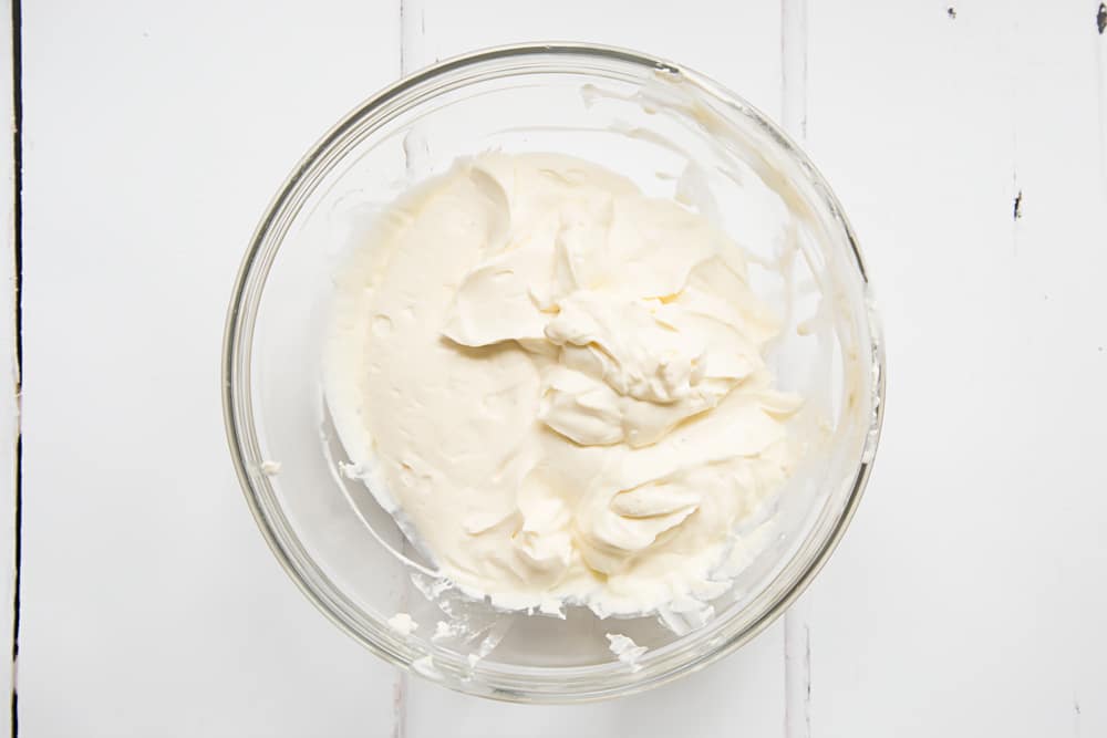 whisked cream cheese, cream and vanilla in a large clear bowl on a white background