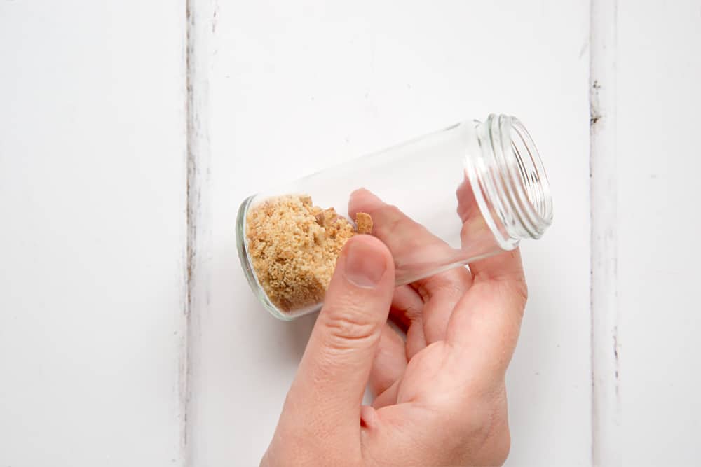 a hand holding a small jar with crushed biscuits in the bottom