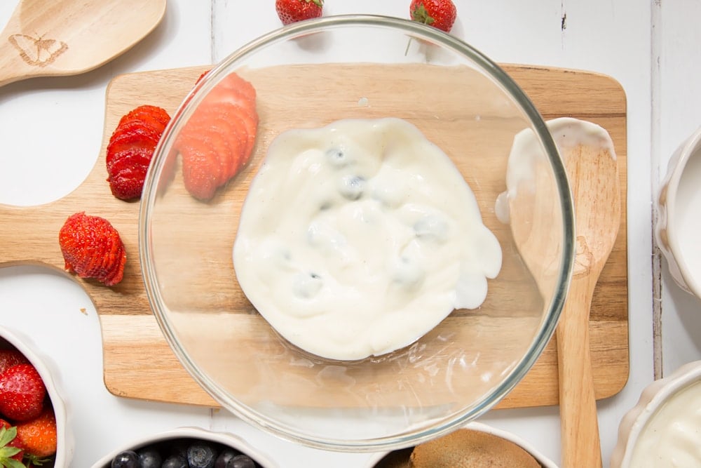 Yogurt is mixed with blueberries, shown alongside thinly sliced strawberries