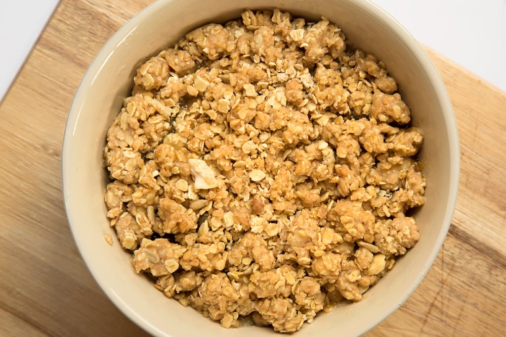 The apple cherry granola crumble in sat on a white bowl on a chopping board.