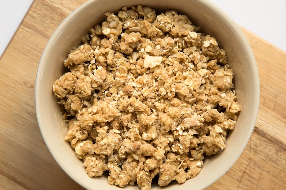 The softened fruit is topped with the crumble topping in a white bowl