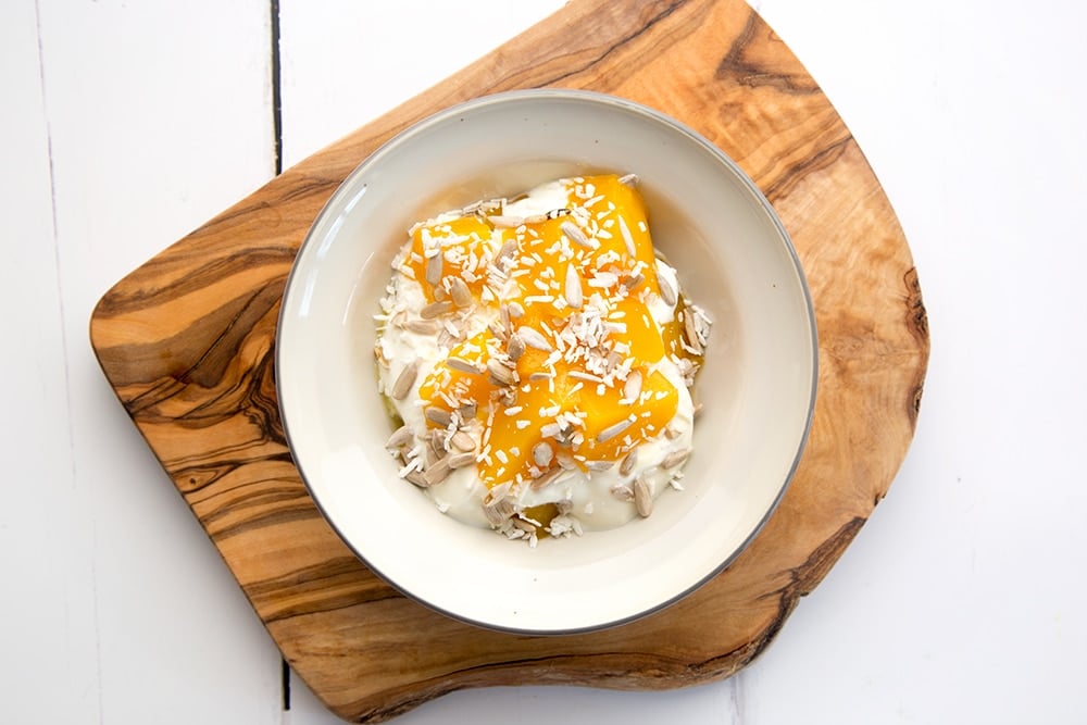 Sprinkle desiccated coconut on top to finish the yogurt and mango breakfast bowls