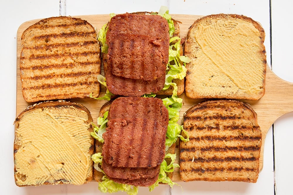 Preparing the deli-style corned beef on rye sandwich by adding lettuce and slices of corned beef, as well as mustard