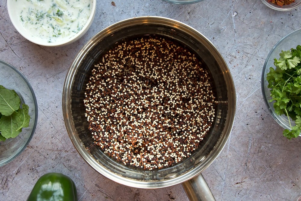 Quinoa being boiled in a saucepan, surrounded by accompaniments to the dish 