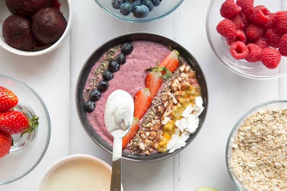 Adding the whipped coconut cream and fresh fruit, like blueberries and strawberries, to the vegan fruit and nut smoothie bowl