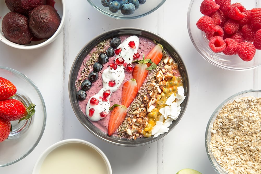 The finished vegan fruit and nut smoothie bowl, topped with seeds, nuts, coconut cream and fresh fruit