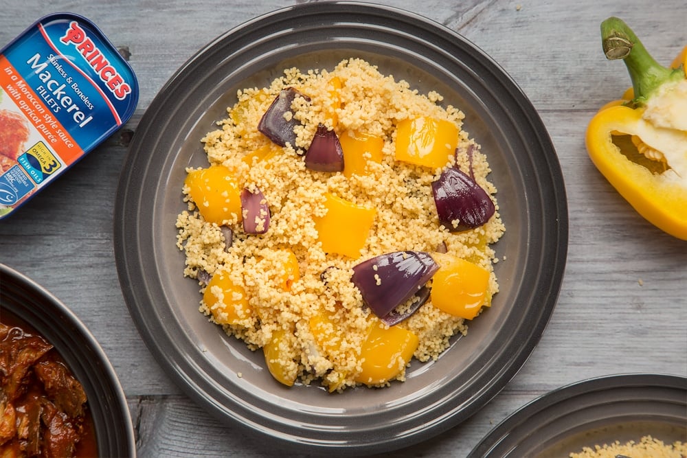 Serve the couscous onto four plates, shown alongside a tin of Princes Mackerel Fillets in a Moroccan Style Sauce with Apricot Purée