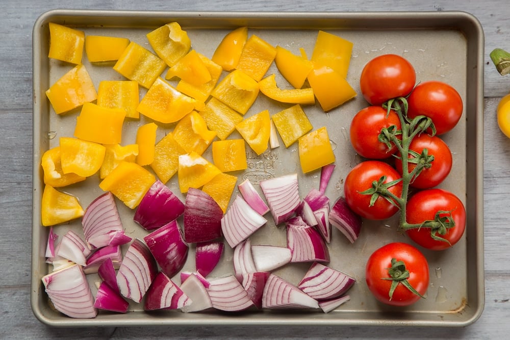 Chopped yellow pepper, red onion and vine tomatoes shown on a baking tray - Moroccan-style mackerel vegetable couscous