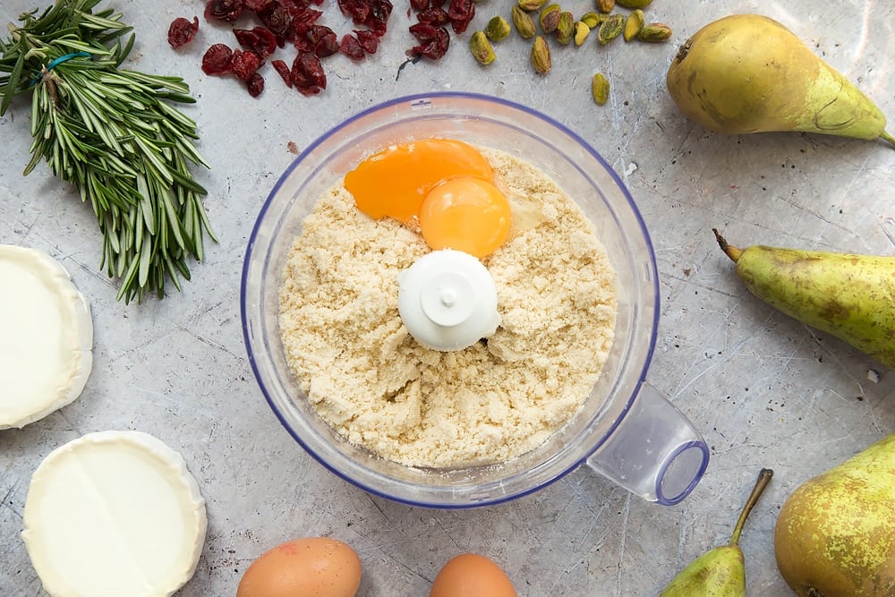 Eggs are added to the mixture, shown in a bowl surrounded by pears, rosemary, pistachios and goat's cheese