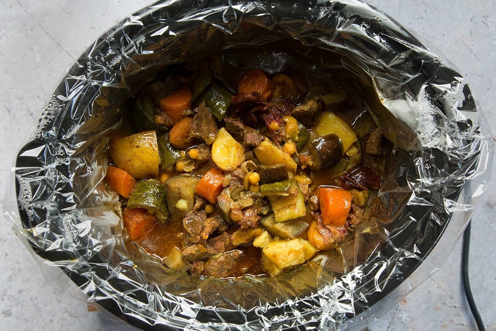 over head shot of a slow cooker with a slow cooker liner and chopped cooked lamb and vegetable pieces.