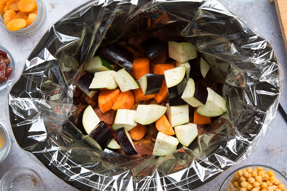 over head shot of a slow cooker with a slow cooker liner and chopped raw vegetable pieces inside.