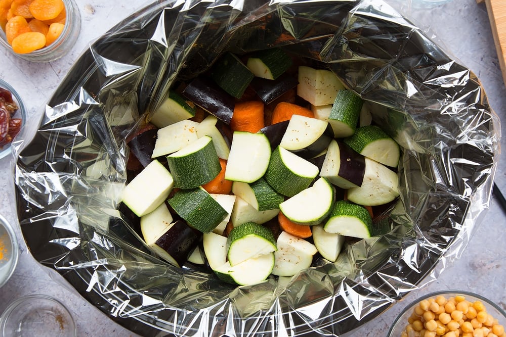 over head shot of a slow cooker with a slow cooker liner and chopped raw vegetable pieces inside.