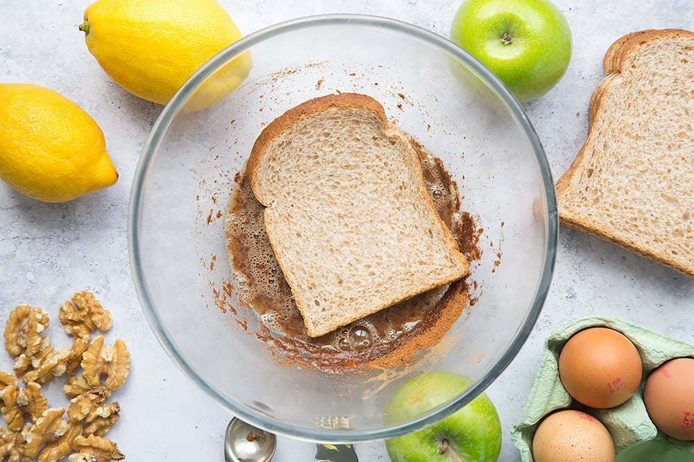 Bread being dipped into the cinnamon batter with ingredients around the edges.