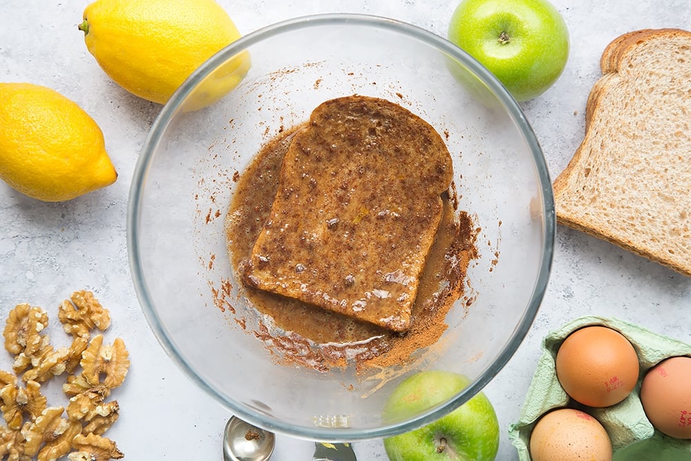 Bread being dipped into the cinnamon batter with ingredients around the edges.