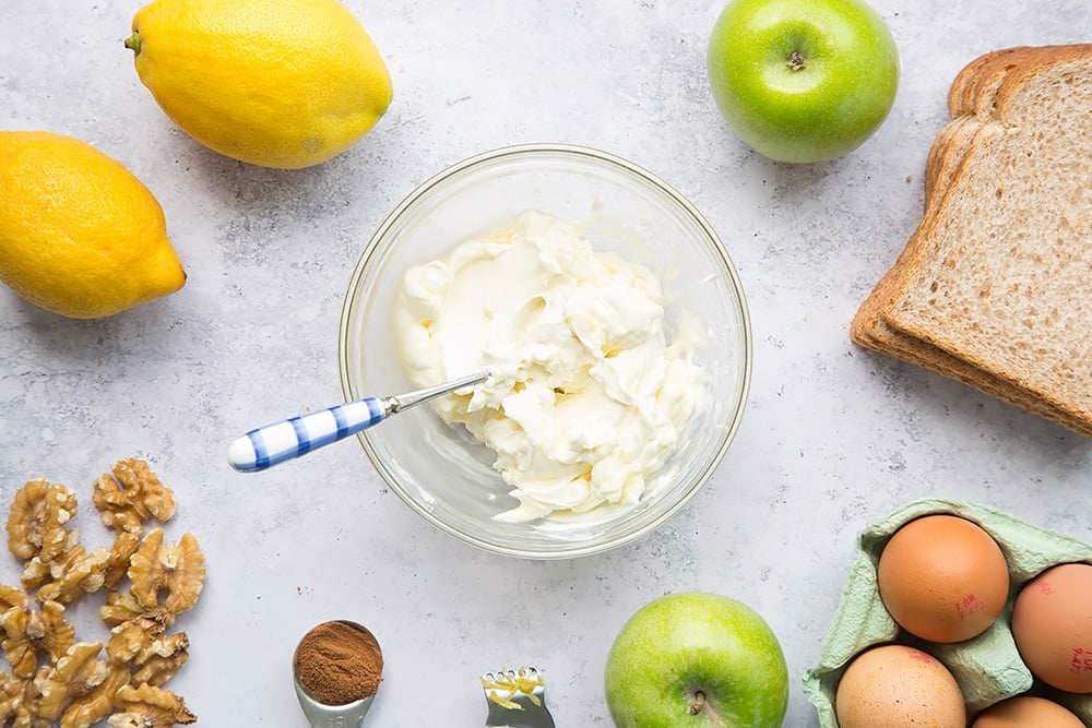 mixed mascarpone, lemon zest, and honey in a bowl surrounded by apples, lemons, eggs and bread.