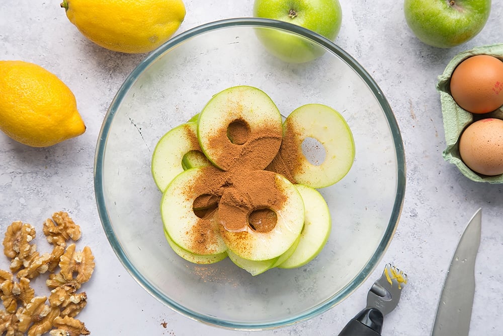 Apple slices, cinnamon and honey in a mixing bowl surrounded by french toast ingredients.