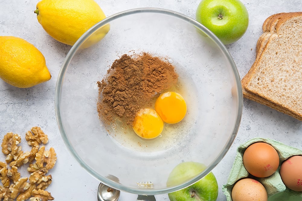 eggs, cinnamon, mixed spice and honey in a clear bowl with ingredients for french toast around the edges.