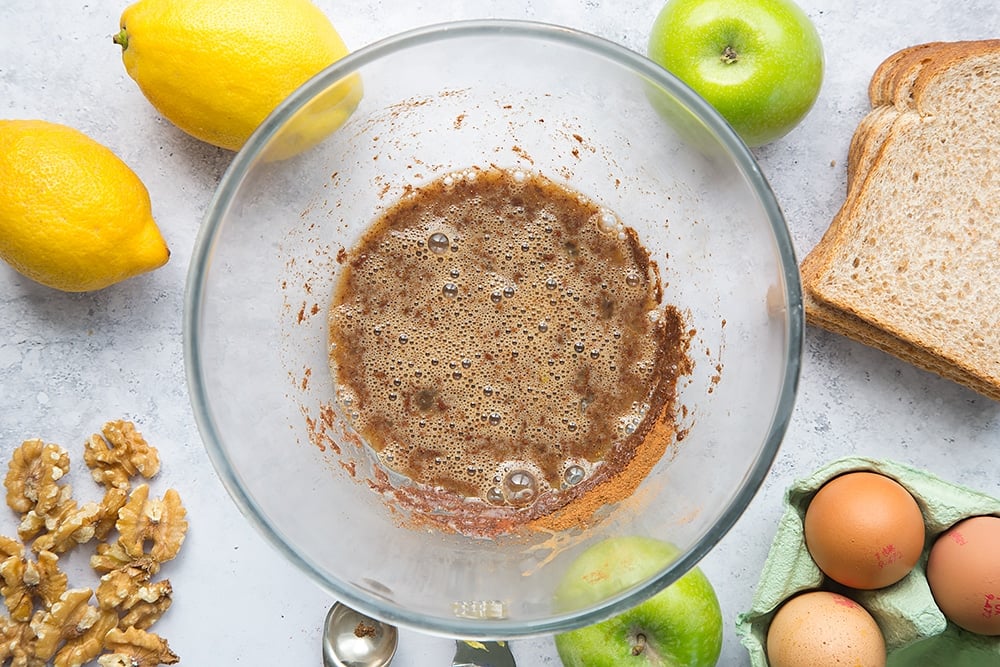 mixed eggs, cinnamon, mixed spice and honey in a clear bowl with ingredients for french toast around the edges.