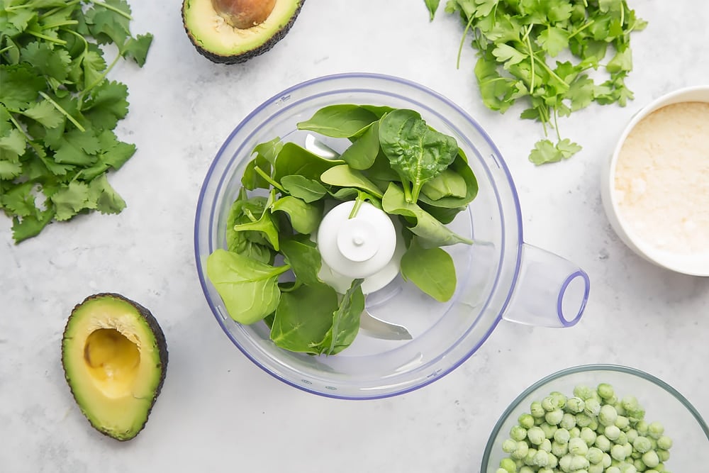 Mixing avocado, peas, spinach, herbs, cheese and milk in a blender