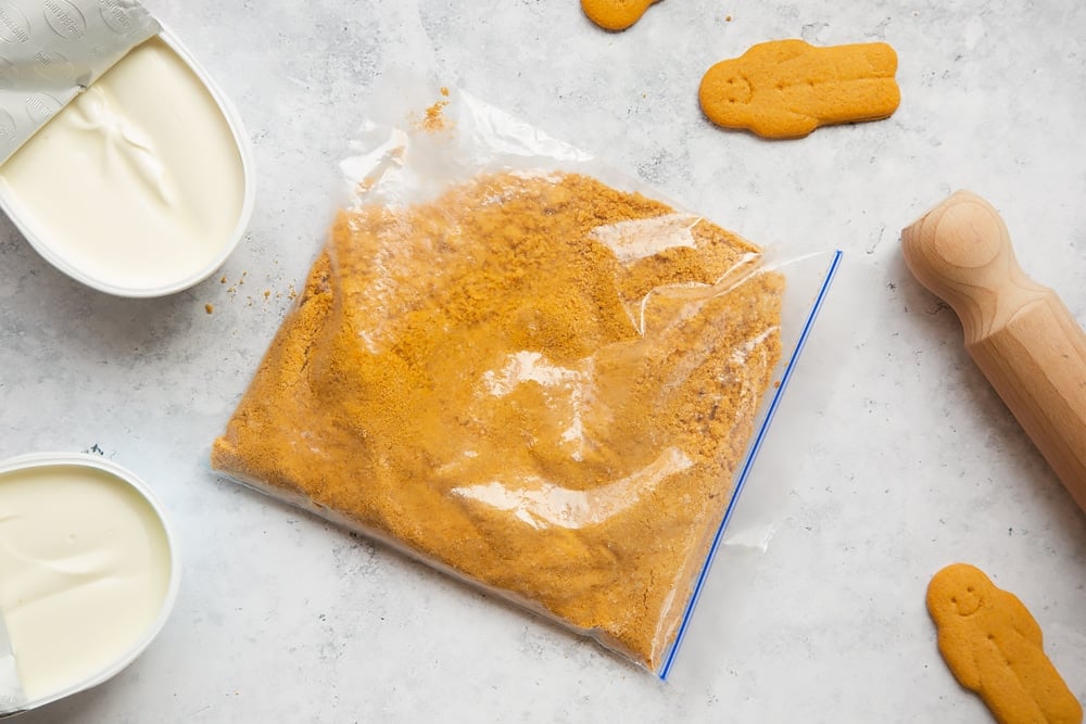 Overhead shot of crushed biscuits inside ziplock bag with a wooden rolling pin on the side