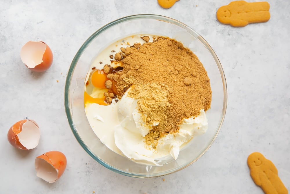 Overhead shot of cream cheese, double cream, sugar, ginger, flour and eggs in a large clear bowl