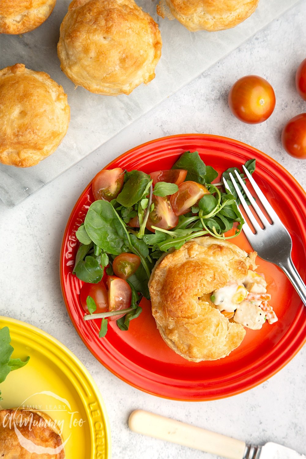 A cut open vegan pie on a red plate with a side salad. At the side there's a yellow plate with the same dish and some additional pies on a marble chopping board.