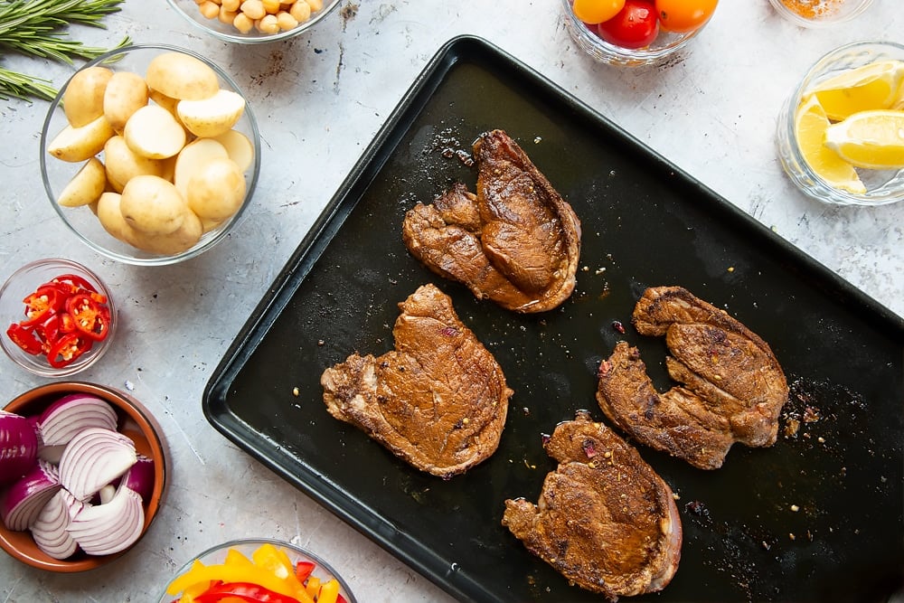 Browning the lamb steaks in a pan before transferring to the sheet tray