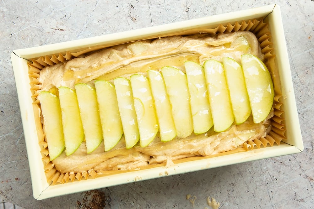 The apple, cinnamon and honey cake in a loaf tin, topped with sliced apples and drizzled with honey 