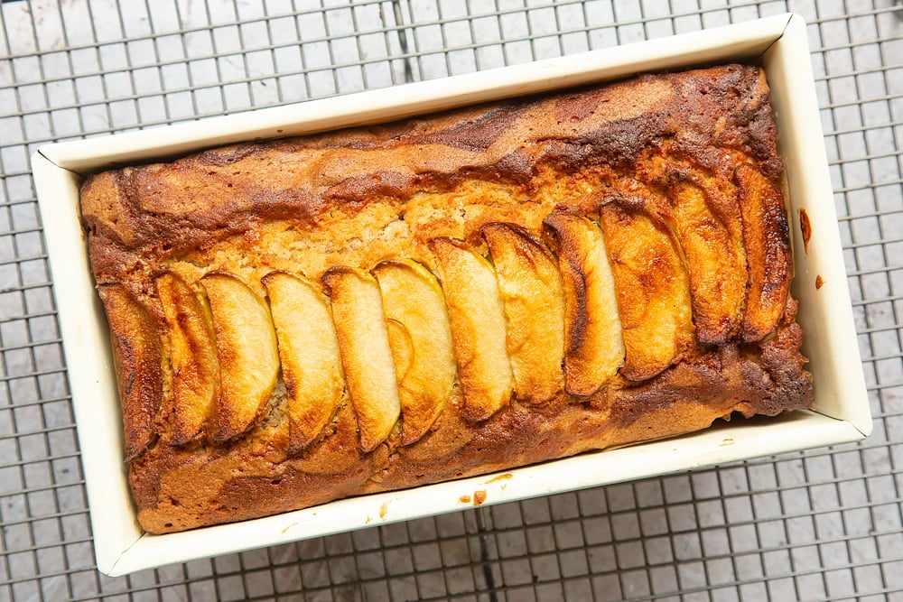 Freshly baked apple, cinnamon and honey cake in a loaf tin cooling on a wire rack