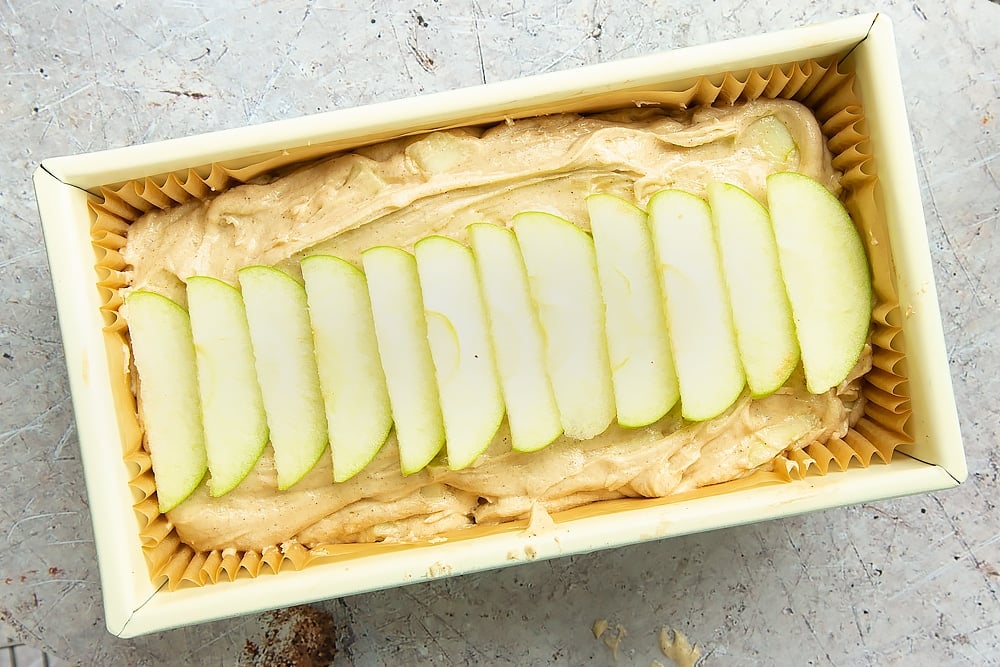 Lining the loaf tin with apple, cinnamon and honey cake batter and topping with sliced apple