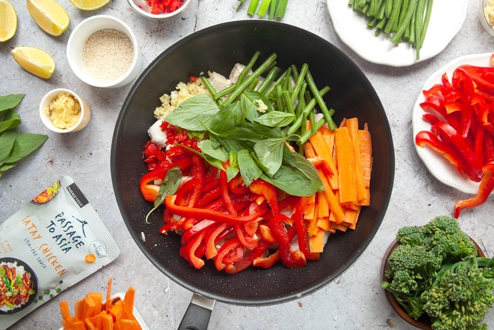 Wok filled with chicken, tofu and colourful vegetables surrounded by chopped vegetables and ingredients.