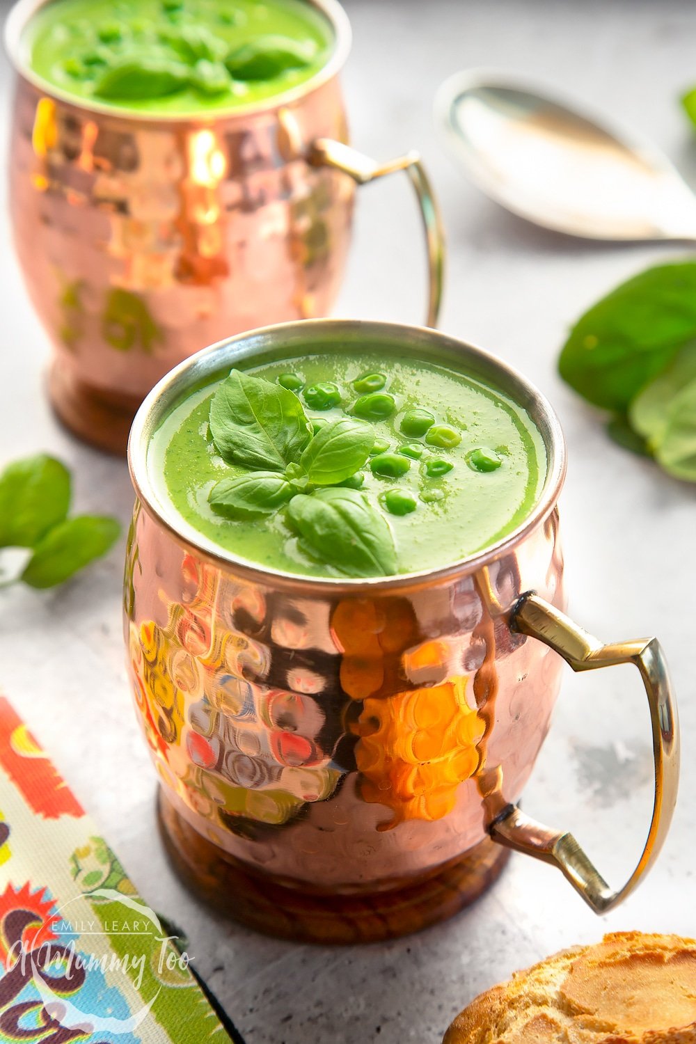 Green soup served in bronze mugs, topped with peas and mint leaves.