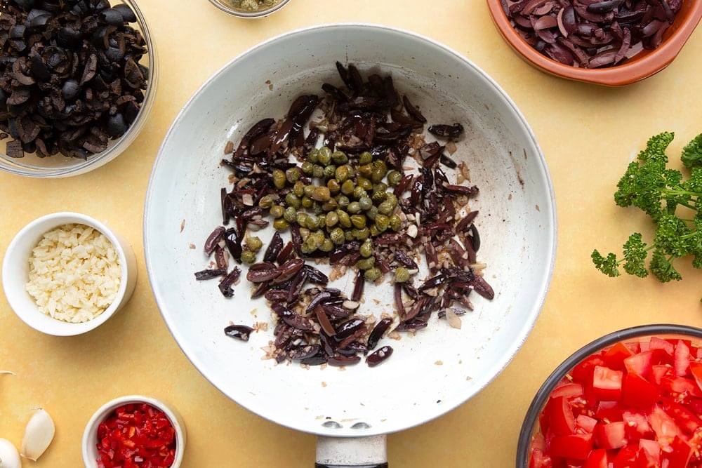 Fried pan contents with a pinch of salt and pepper ready to create spaghetti alla puttanesca