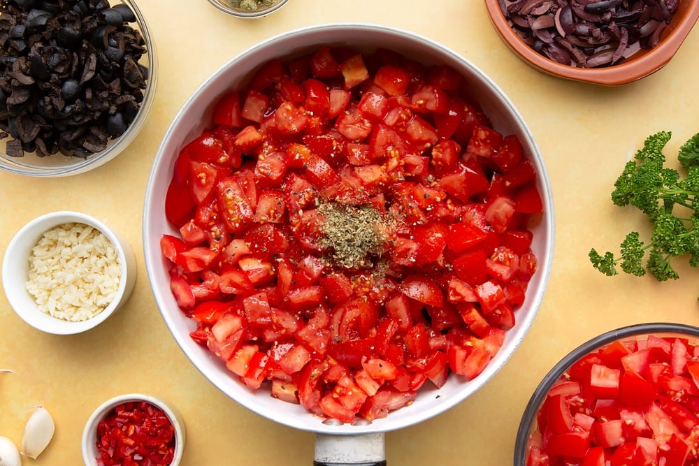 spaghetti alla puttanesca pan contents with diced tomatoes on top