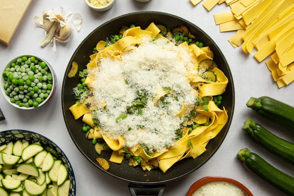 Courgettes, peas, fresh mint, and lasagne pasta strips stirred together in a frying pan. Parmesan added.