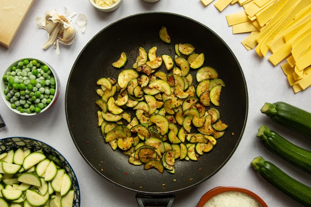 Garlic, oil, chilli flakes and courgettes fried in a frying pan.