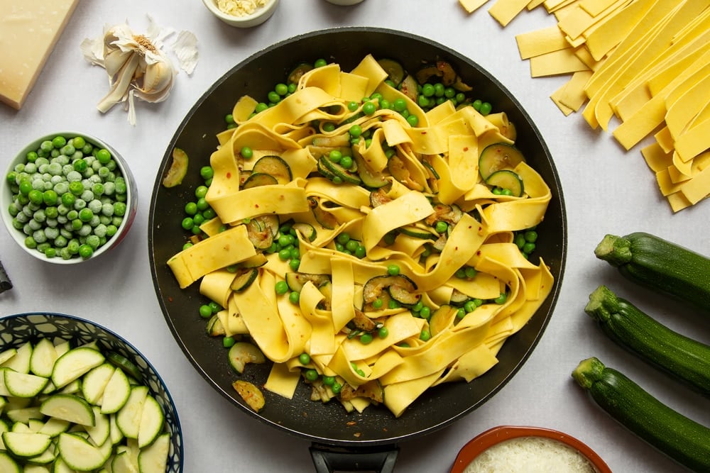 Courgettes, peas and lasagne pasta strips stirred together in a frying pan.