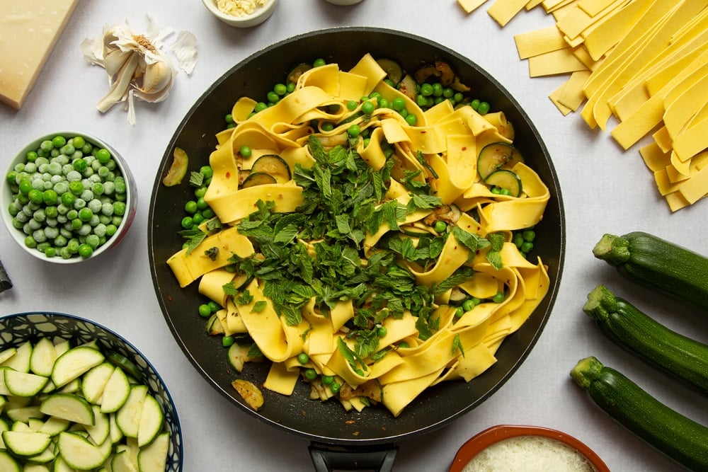 Courgettes, peas and lasagne pasta strips stirred together in a frying pan. Mint leaves added.