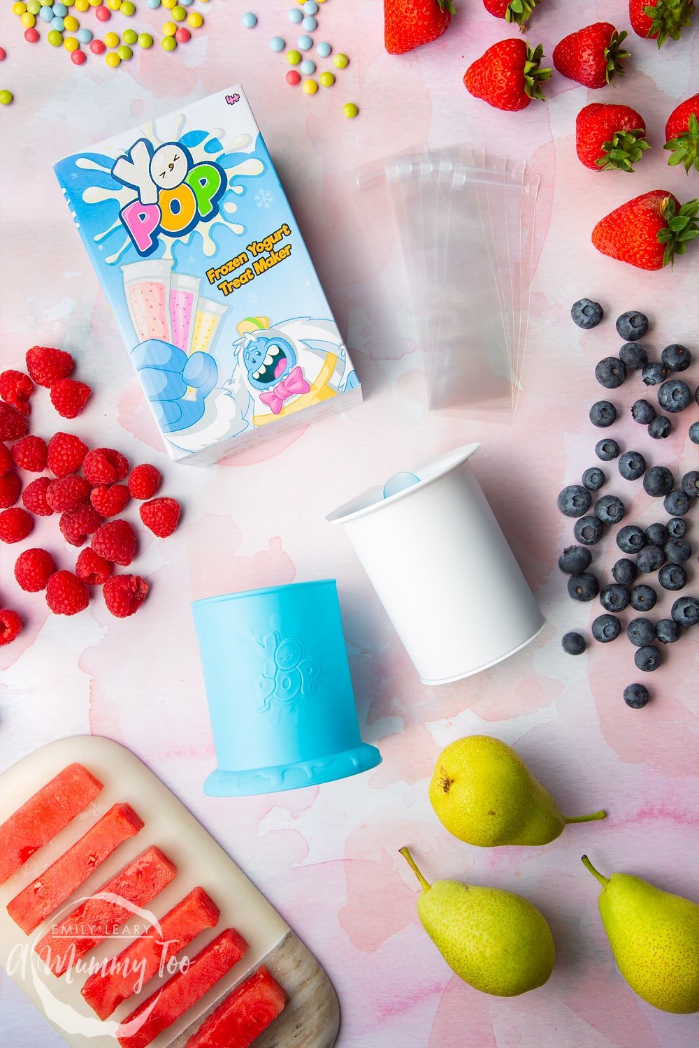 YoPop frozen yogurt maker laid out on a pink surface surrounded by fruit.