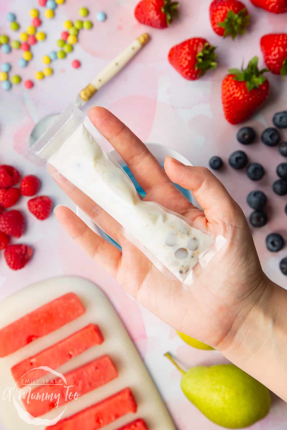 hand holding a yogurt fruit ice pop before freezing with fruit in the background.