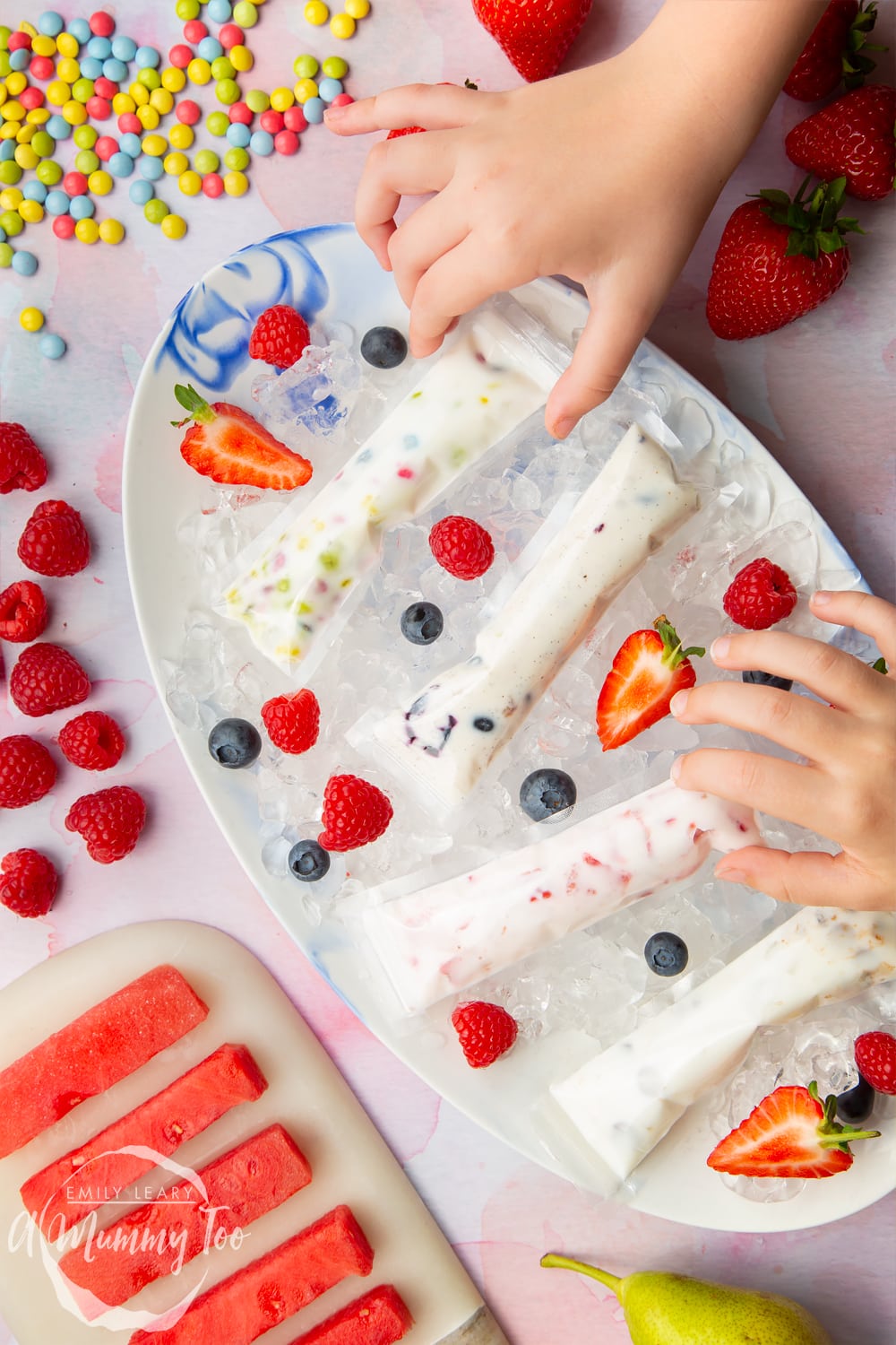 hands picking up a Frozen yogurt treat ideas with YoPop from a plate surrounded by sweets and strawberries